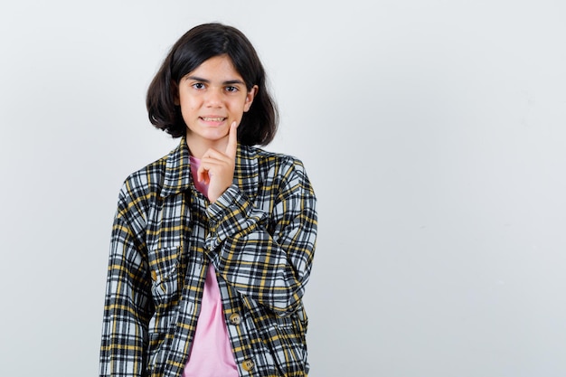 Garota pré-adolescente apontando para o sorriso dela na camisa, jaqueta, vista frontal.