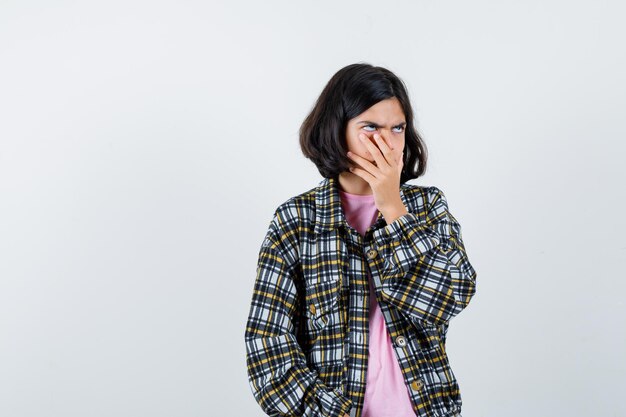 Garota pré-adolescente bocejando com a mão na boca na camisa, jaqueta e parecendo com sono, vista frontal.