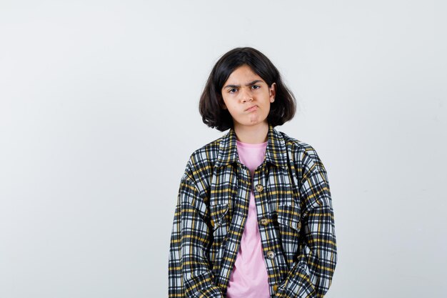 Garota pré-adolescente olhando para a câmera em camisa, jaqueta e parecendo nervosa, vista frontal.