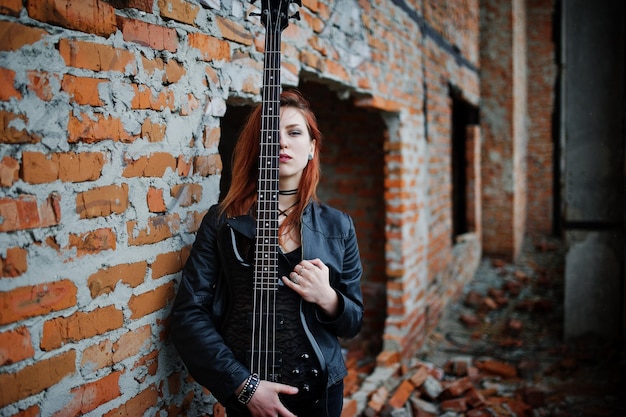 Foto grátis garota punk de cabelo vermelho usa preto com baixo em lugar abandonado retrato de músico de mulher gótica feche o rosto de uma pessoa negra com riff de guitarra