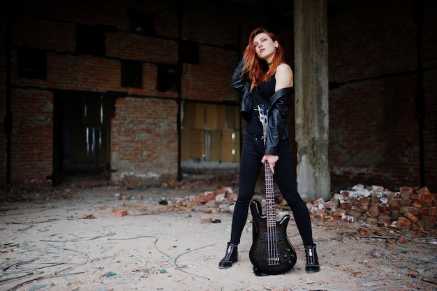 Garota punk de cabelo vermelho veste preto com guitarra baixo em lugar abandonado Retrato de músico gótico