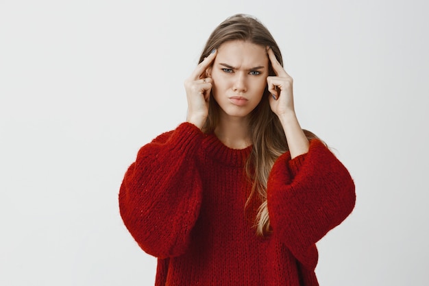 Foto grátis garota puxando todos os esforços para encontrar solução ou lembrar de algo. retrato de mulher jovem problemática focada, segurando os dedos indicadores em templos e franzindo a testa, tentando se concentrar na questão sobre parede cinza