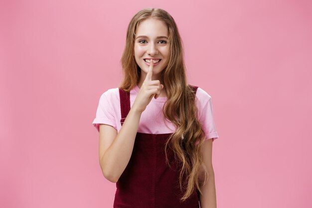 Garota quer compartilhar seu segredo de beleza sorrindo complicado e amigável, mostrando um gesto de silêncio com o dedo indicador ...