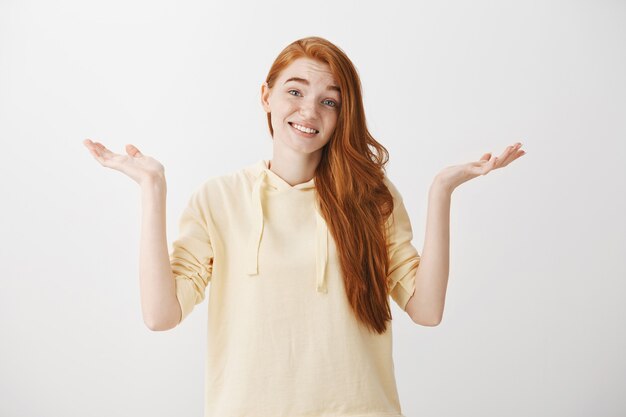 Garota ruiva confusa e indecisa dando de ombros com um sorriso forçado