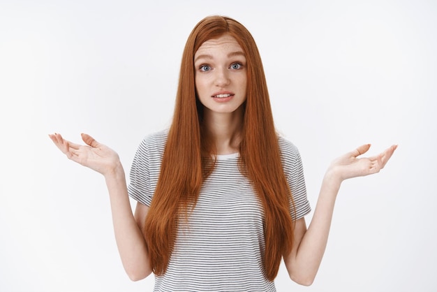 Foto grátis garota ruiva, sem noção e sem noção, olhos azuis vestindo camiseta de verão, encolhendo os ombros, não tenho ideia, não posso responder, pareça perplexo, questionado, levante as mãos de lado em pé fundo branco copiar espaço