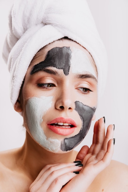 Garota sem maquiagem faz sua rotina matinal na parede branca. Lady usa máscara de argila para melhorar a pele.