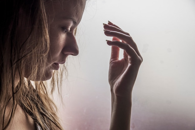 Foto grátis garota solitária perto da janela pensando em algo. mulher triste olhando a chuva caindo através de uma janela em casa