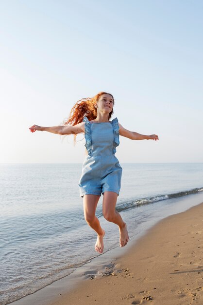 Foto grátis garota sorridente de tiro completo pulando na praia