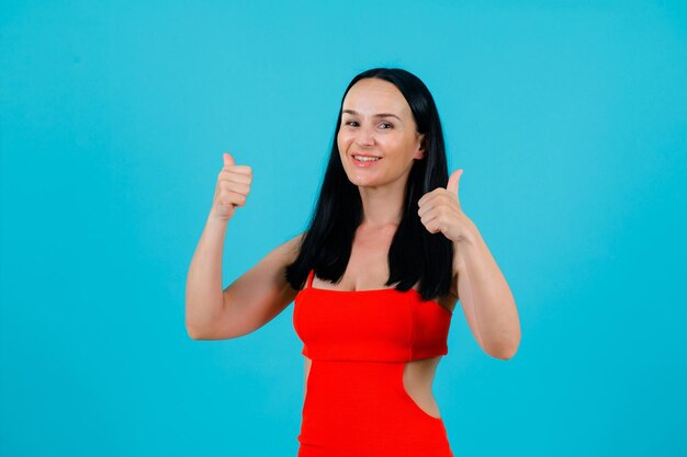 Garota sorridente está olhando para a câmera mostrando gestos perfeitos com polegares sobre fundo azul