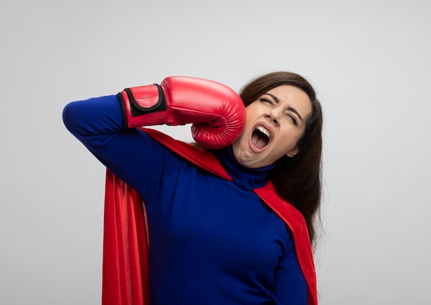 Garota super-heroína caucasiana irritada com capa vermelha usando luvas de boxe