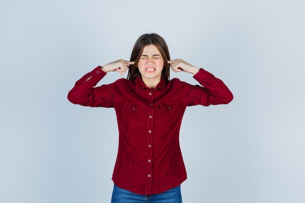 garota tapando as orelhas com os dedos em uma camisa casual e parecendo irritada