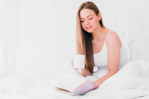 Garota tomando café com um livro na cama