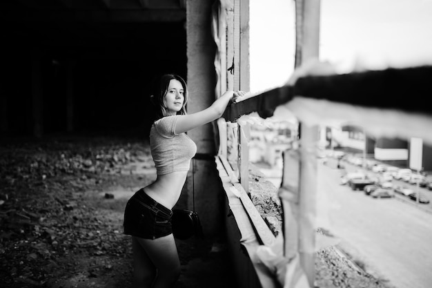 Garota usa shorts em fábrica abandonada com paredes de tijolos