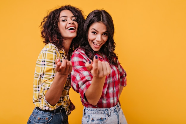 Garotas alegres sugerem abordá-los. Retrato de morenas alegres e sorridentes em roupas elegantes