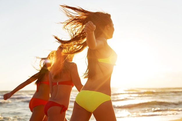 Garotas correndo na praia, tendo uma festa no fundo dourado do pôr do sol de verão