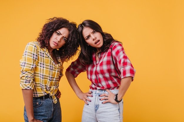 Garotas de olhos castanhos olham com indignação e condenação. instantâneo de amigos insatisfeitos com camisetas semelhantes.