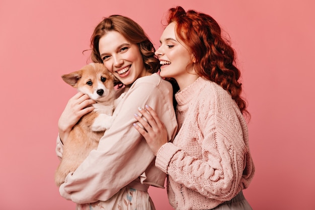 Foto grátis garotas maravilhosas segurando cachorro bonito isolado no fundo rosa. foto de estúdio de sorridentes senhoras europeias posando com animal de estimação.