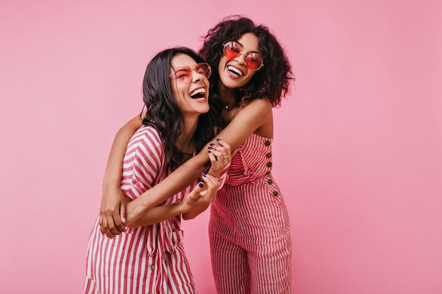 Garotas sinceras com sorriso radiante posam em um macacão rosa listrado. foto de verão de modelos engraçados.