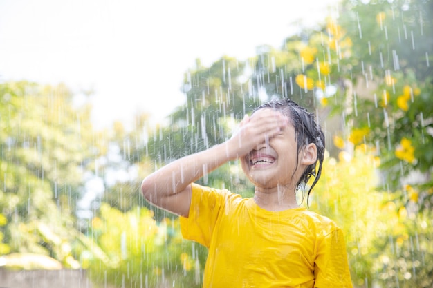 Garotinha asiática feliz se divertindo e brincando com a chuva ao sol
