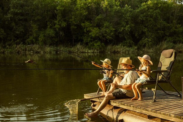 Garotinhas lindas e o avô estão pescando no lago ou rio