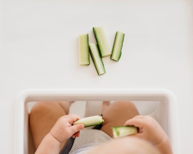 Foto grátis garotinho na cadeira de bebê segurando pedaços de pepino