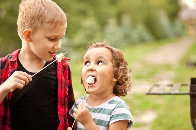 Garoto adolescente e garoto garota comendo marshmalloy assado ao ar livre em um acampamento. viagem, caminhada, férias, conceito de acampamento.