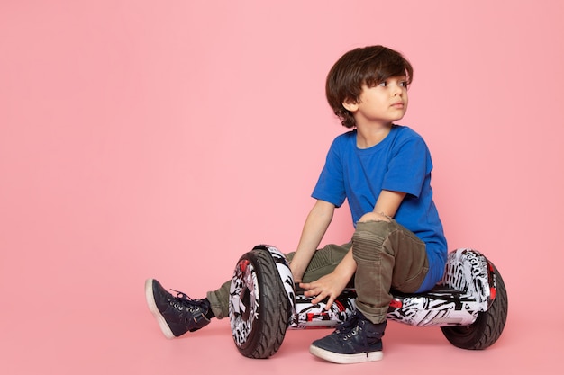 Garoto adorável bonito na camiseta azul andando segway na parede rosa