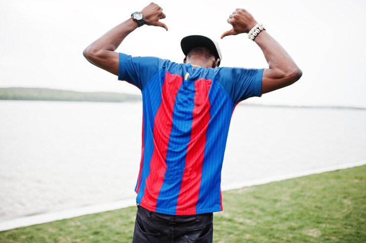 Foto grátis garoto afro-americano estiloso usa camiseta de futebol de boné mostrando as costas contra o lago retrato de homem esportivo negro