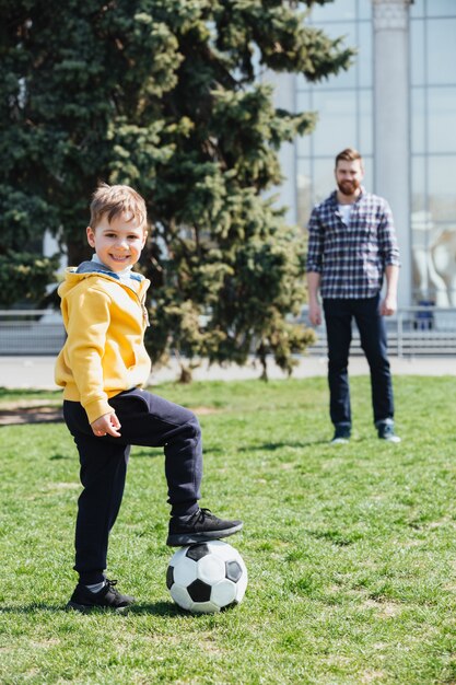 Garoto bonito jogando futebol com seu pai no parque