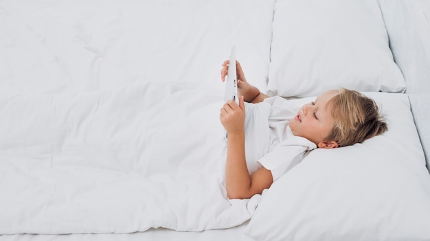 Foto grátis garoto de alto ângulo assistindo algo em um tablet na cama