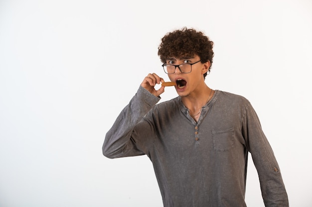 Garoto de cabelo encaracolado em óculos de lentes grandes abre os olhos e a boca para comer biscoito.