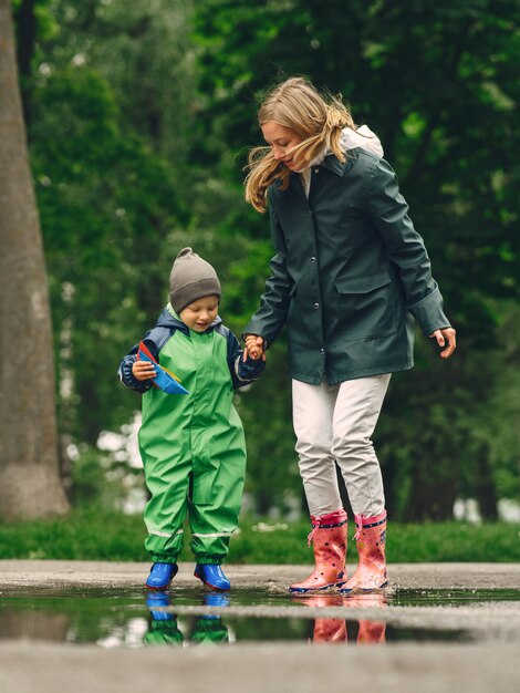 Garoto engraçado em botas de chuva, jogando em um parque de chuva