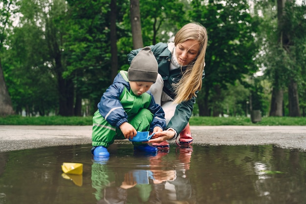 Garoto engraçado em botas de chuva, jogando em um parque de chuva