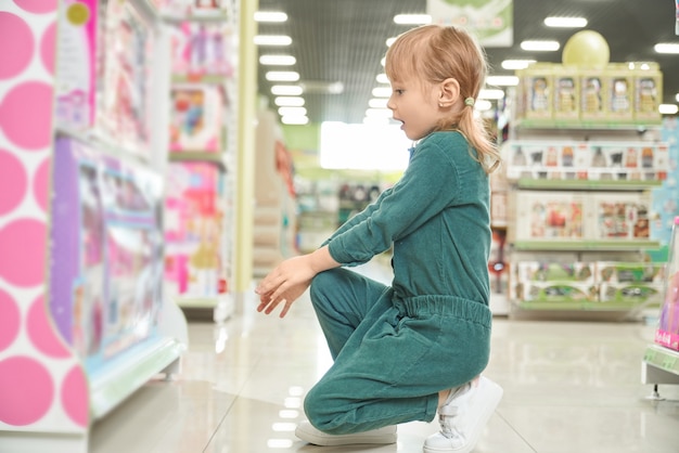 Garoto espantado, sentado perto de stands com brinquedos e escolhendo bonecas