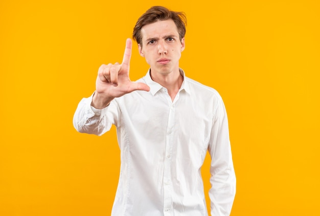 Garoto jovem e rigoroso vestindo camisa branca e mostrando gesto de perdedor isolado na parede laranja