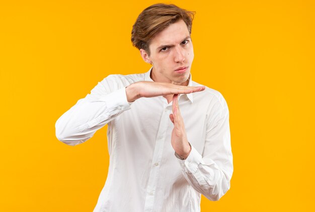 Garoto jovem e rigoroso vestindo uma camisa branca e mostrando o gesto de tempo limite isolado na parede laranja