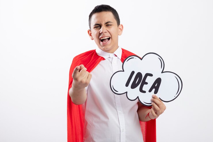 Foto grátis garoto jovem super-herói confiante com capa vermelha segurando uma bolha de ideia, olhando e apontando para a câmera isolada no fundo branco com espaço de cópia