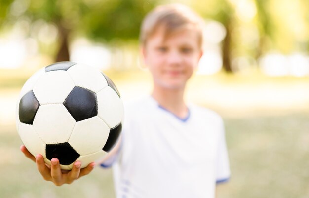 Garoto loiro sem foco segurando uma bola de futebol