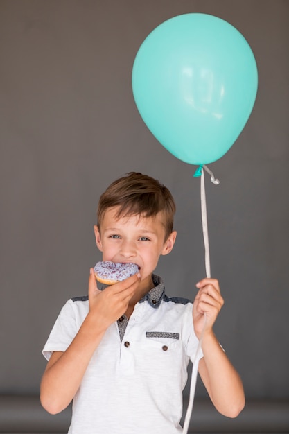 Garoto segurando um balão enquanto come um donut