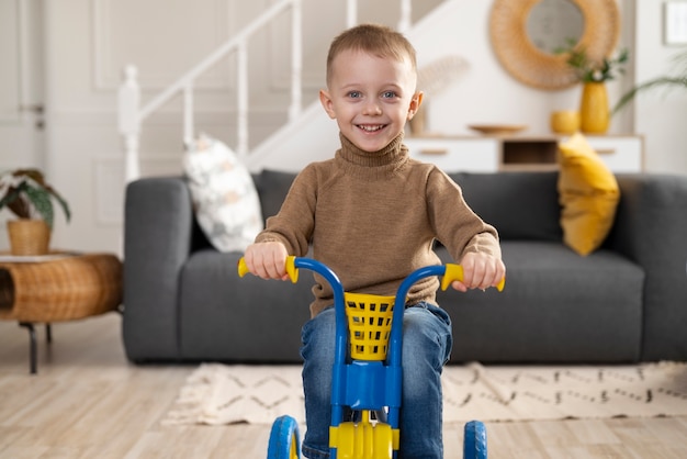 Foto grátis garoto sorridente de tiro completo sentado no triciclo dentro de casa