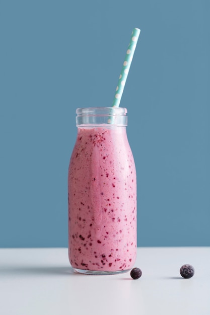 Garrafa de smoothie rosa vista frontal com palha e mirtilos