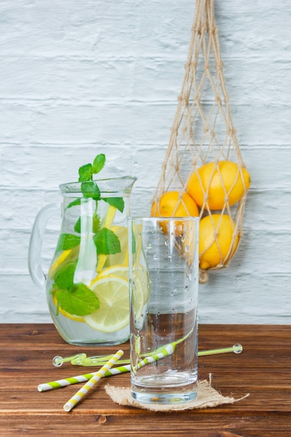 Garrafa de vista lateral de limão com canudos, copo vazio na superfície de madeira e branca. espaço vertical para texto