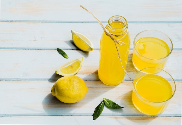 Garrafa e copos com coquetel de limão na mesa de madeira gasto