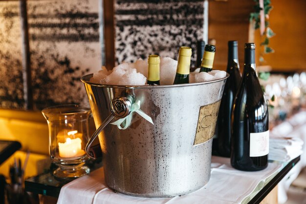 Garrafas com champanhe estão esfriando no balde com gelo e garrafas com vinho estão próximas