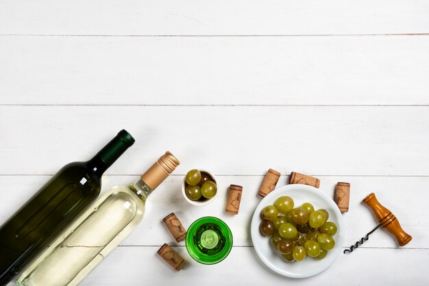 Garrafas de vinho branco ao lado de rolhas e uvas