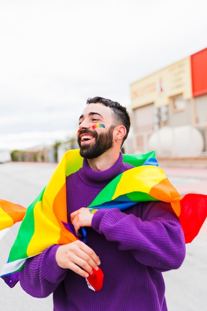 Gay com bandeira de arco-íris sorrindo na rua