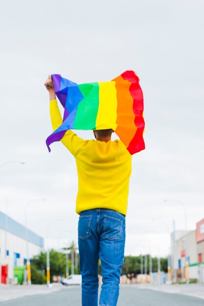 Gay indo na estrada segurando bandeira LGBT sobre a cabeça