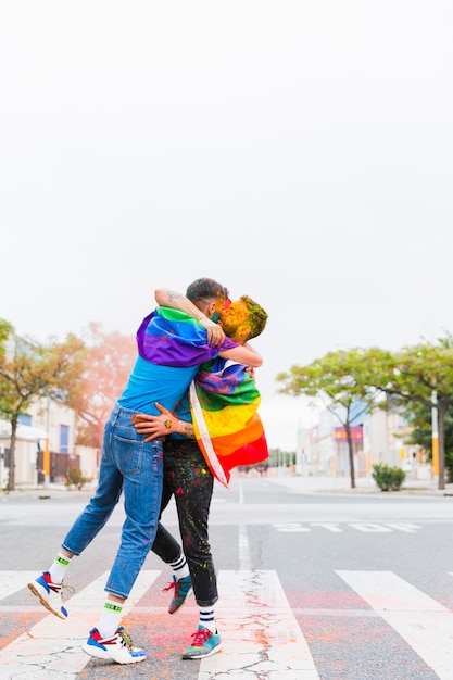Gays com bandeiras de arco-íris abraçando na passagem para pedestres