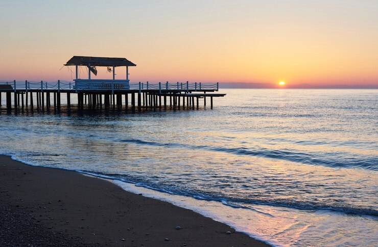 Foto grátis gazebo no cais de madeira para o mar com o sol ao pôr do sol.