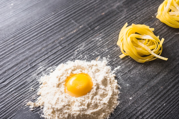 Gema de ovo com farinha branca e tagliatelle cru em pano de fundo preto de madeira